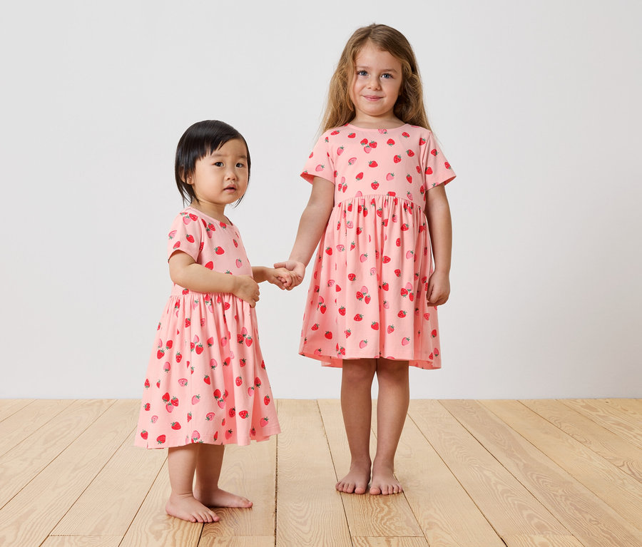 Deux filles se tiennent la main et portent des robes roses à fraises.