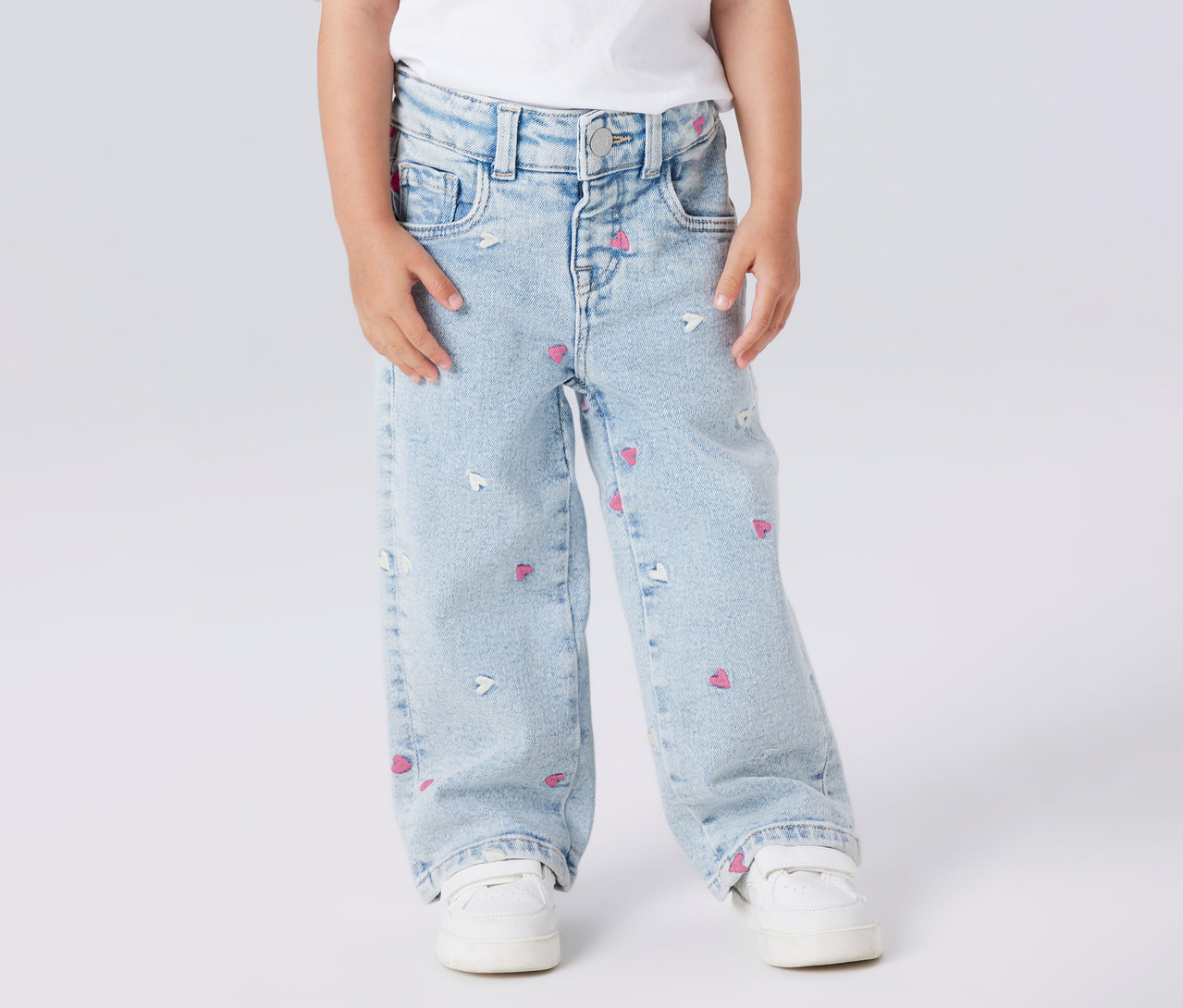 Un enfant porte un jean à jambes larges NAME IT avec un motif de cœur et des chaussures blanches.