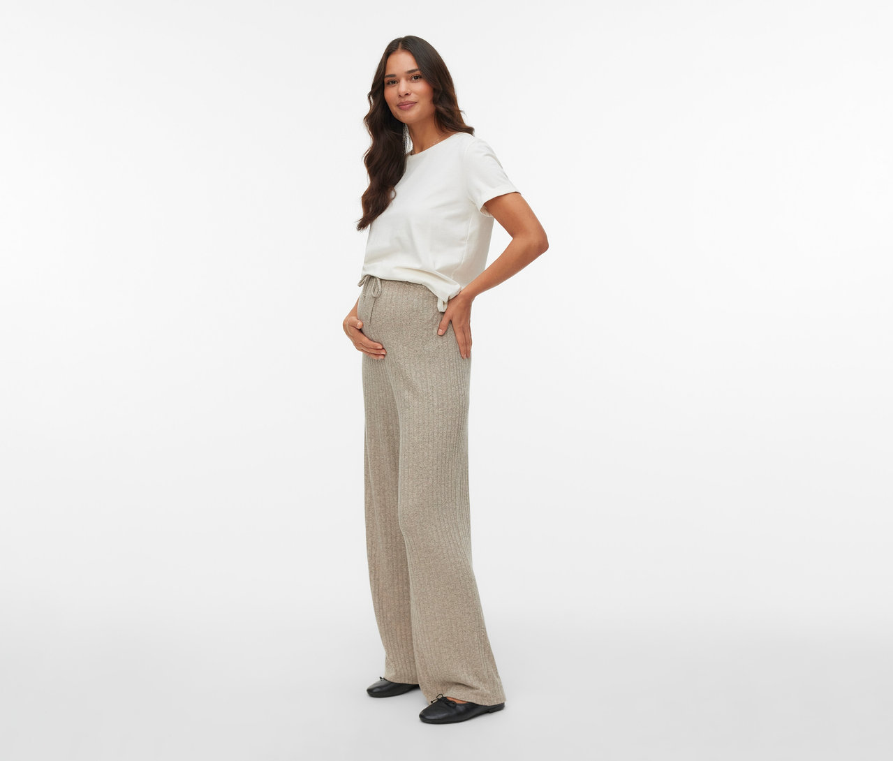 Femme enceinte posant en pantalon Loosefit MAMALICIOUS « MLPAMMIE » et t-shirt blanc, la main sur le ventre.