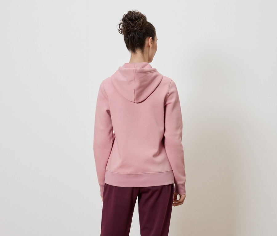 Vue arrière d'une femme portant un chignon, un sweat à capuche rose et un pantalon bordeaux sur un fond blanc.
