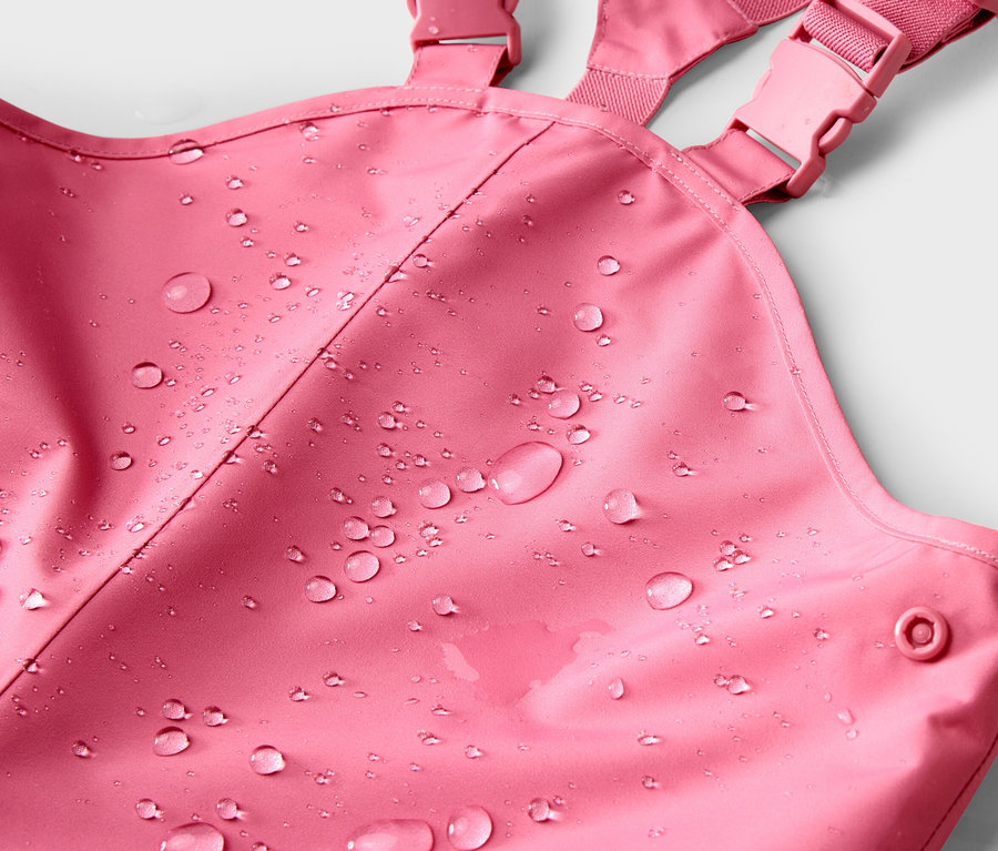 Gros plan sur une salopette de pluie rose avec des gouttes d'eau sur le tissu.