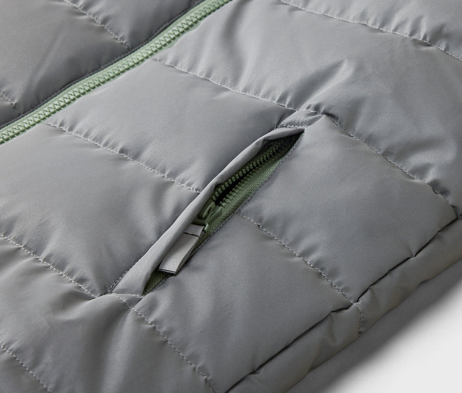 Gros plan sur un gilet matelassé gris avec une fermeture éclair verte sur la poche.