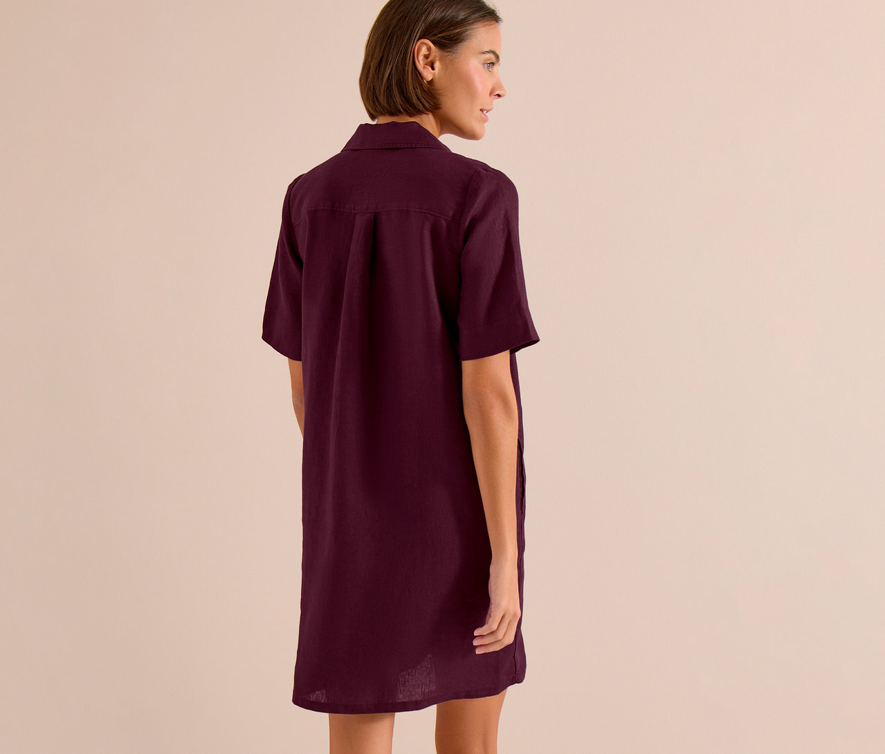 Une femme aux cheveux courts bruns porte une robe chemise bordeaux, vue de dos.