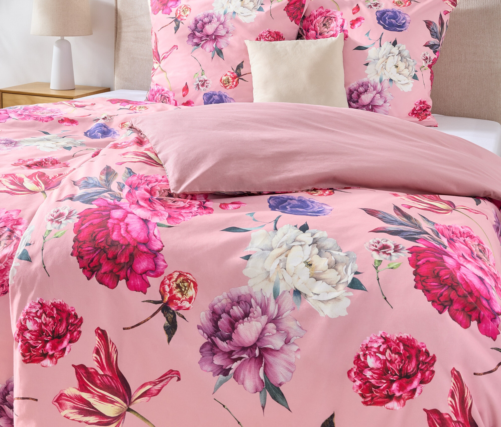 Gros plan d'un lit avec des draps roses à motif floral, une tête de lit beige et deux images encadrées au mur.