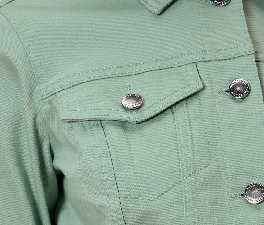 Gros plan sur une veste vert clair avec des boutons argentés et une poche poitrine.
