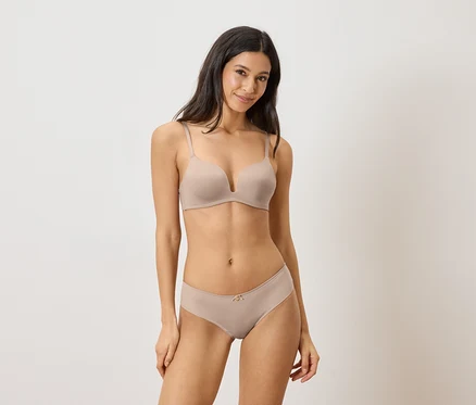 Femme portant un soutien-gorge push-up beige et une culotte assortie, souriant à la caméra.