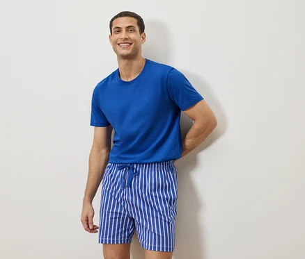 Homme portant un t-shirt bleu et un short rayé debout devant un mur blanc.