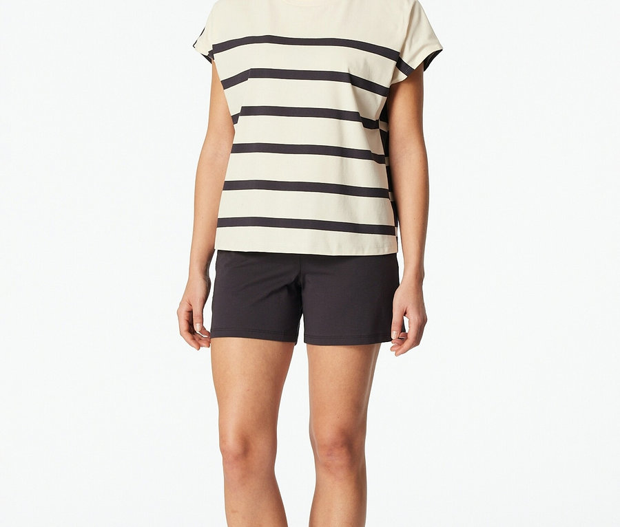 Une femme se tient pieds nus sur un fond blanc, vêtue d'un haut rayé et d'un short noir.