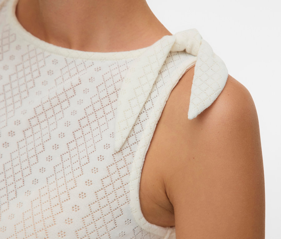 Gros plan d'une femme portant un haut sans manches blanc en broderie anglaise avec un nœud sur l'épaule.