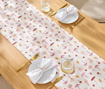 Table avec un chemin de table à motif de champignons, des couverts dorés, une serviette en tissu blanche et un verre d'eau.