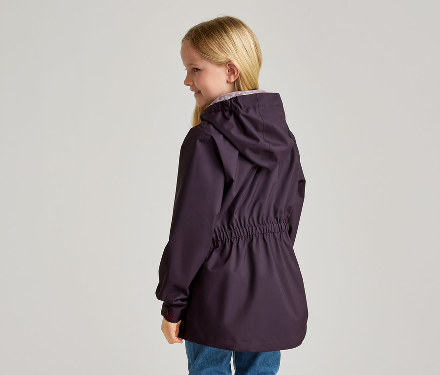 Une jeune fille blonde de profil porte une veste violet foncé à capuche avec cordon de serrage à la taille et un jean bleu.