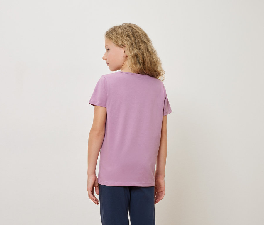 Vue arrière d'une blonde portant un t-shirt violet et un pantalon bleu sur un fond blanc.
