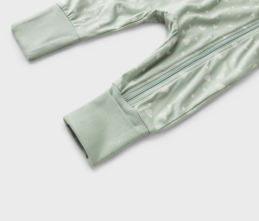 Gros plan d'une grenouillère vert clair pour bébé avec un motif de cœurs blancs et une fermeture éclair sur toute la longueur.