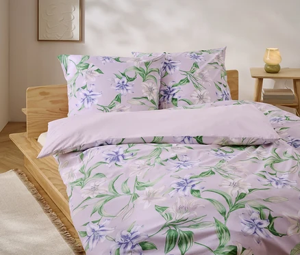 Lit avec des draps lilas à motif floral et un cadre de lit en bois.