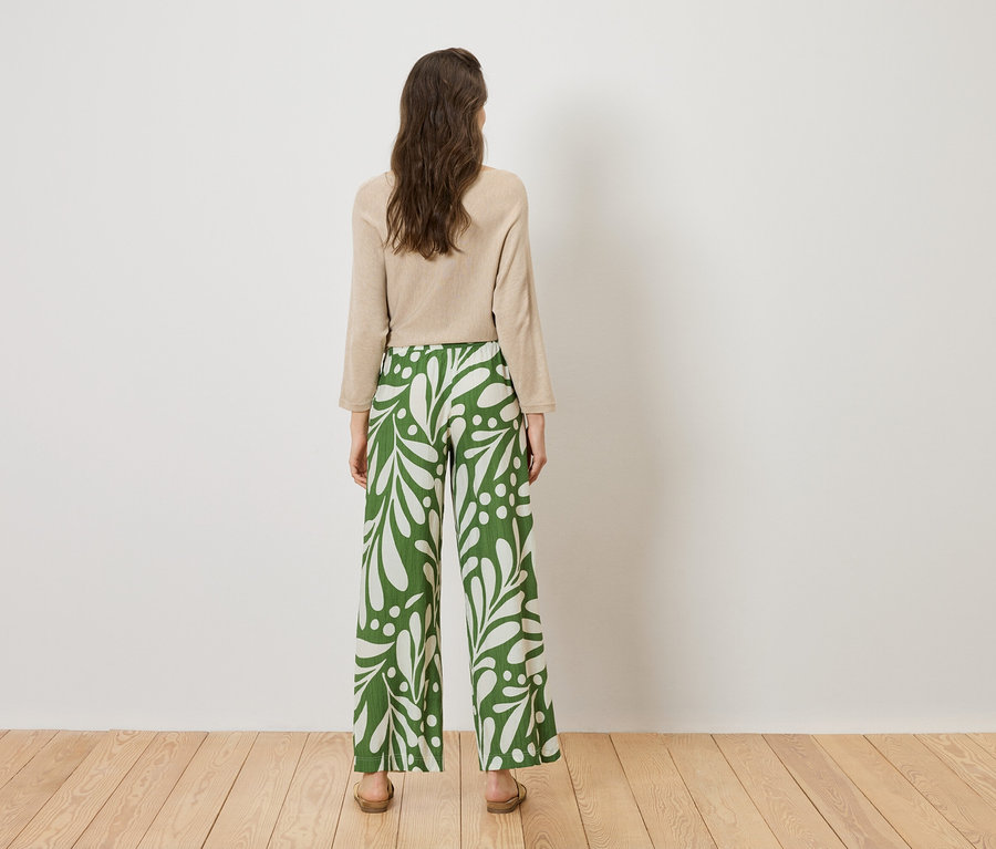 Vue arrière d'une femme portant un haut beige et un pantalon à motifs vert et blanc.