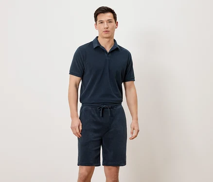 Un homme porte un polo bleu marine et un short bleu marine.