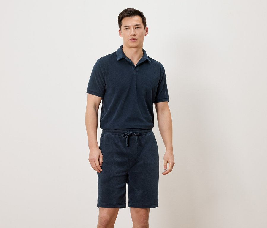 Un homme porte un polo bleu marine et un short bleu marine.
