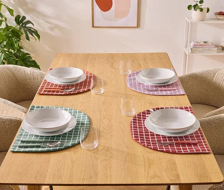 Une table à manger avec quatre couverts composés d'assiettes, de bols, de couverts et de verres sur des sets de table à carreaux.