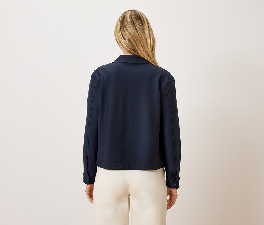 Vue arrière d'une femme aux cheveux blonds portant une veste bleu marine et un pantalon couleur crème.