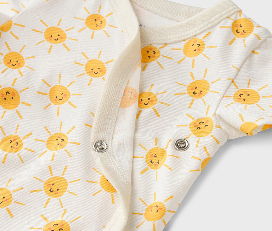 Gros plan d'un body bébé blanc avec un motif de soleils jaunes et des boutons-pression.