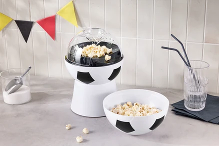Une machine à pop-corn en forme de ballon de football se trouve à côté d'un bol de pop-corn et d'un verre avec des pailles.