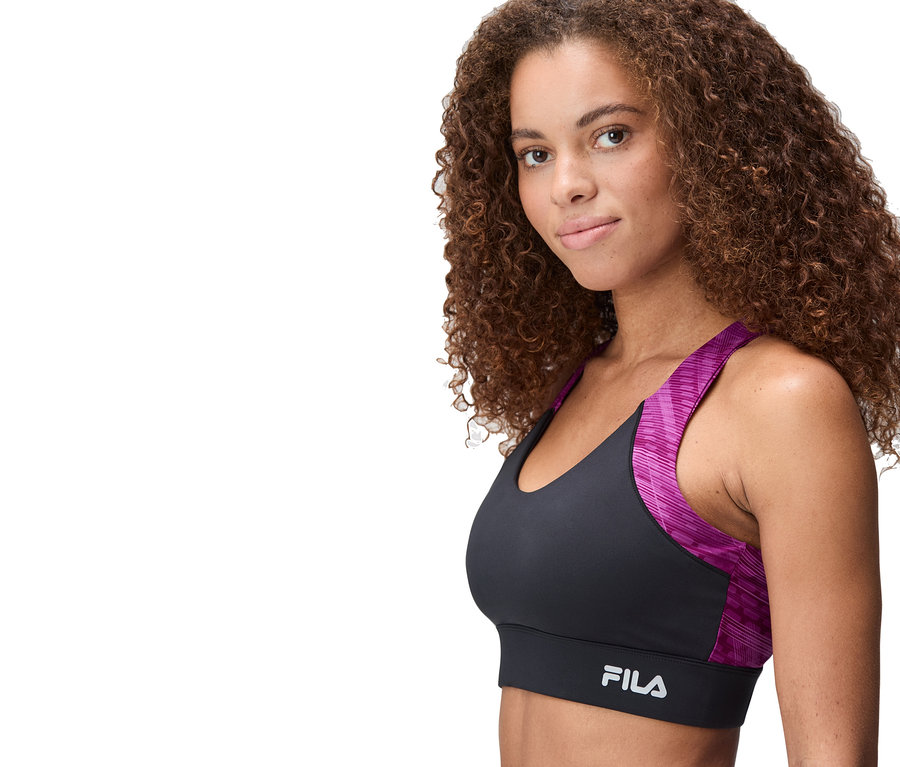 Une femme porte une brassière de sport noire et rose de la marque FILA.