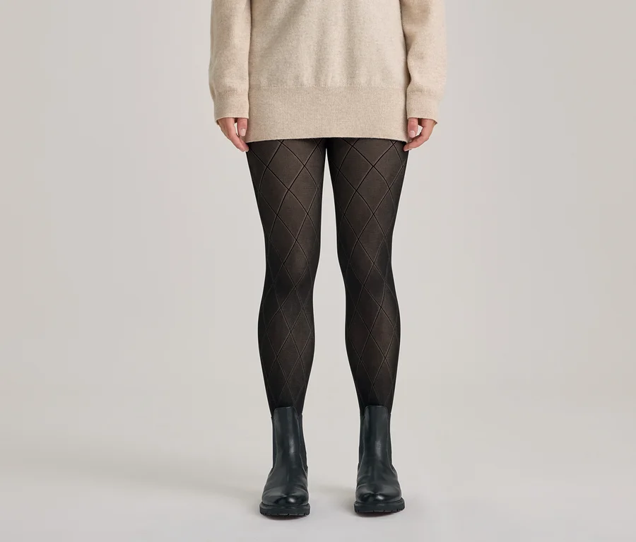 Personne portant un pull beige, un collant noir à motif losanges et des bottines noires.