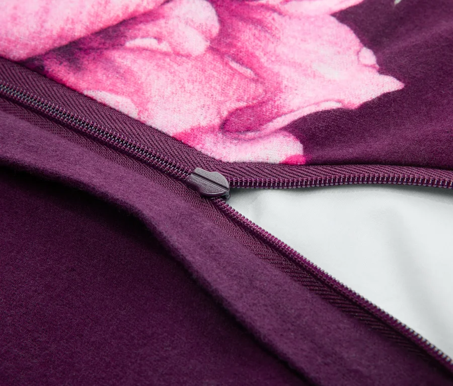 Gros plan d'une fermeture éclair violet foncé partiellement ouverte sur un tissu, révélant une doublure blanche. Le tissu présente une section violet foncé et un motif floral rose.