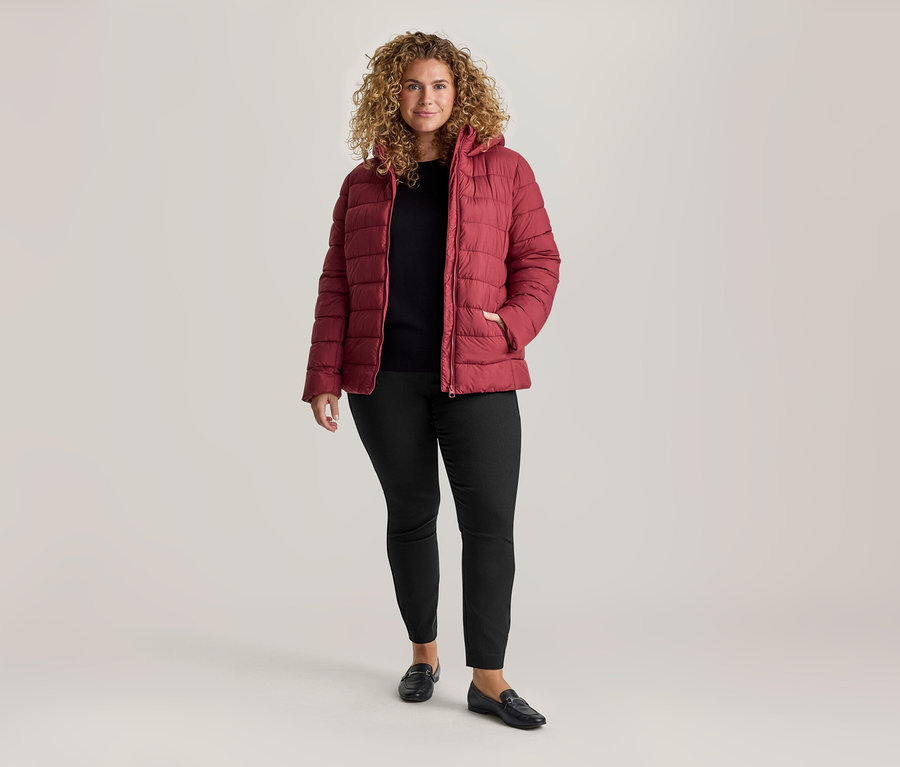 Femme aux cheveux bouclés, portant une doudoune rouge, un haut noir et un pantalon stretch noir.