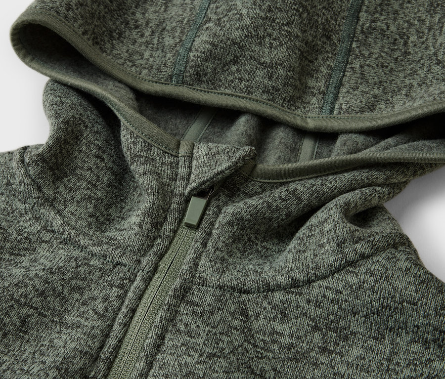 Gros plan d'un sweat à capuche vert chiné avec une fermeture éclair, posé sur une surface blanche.