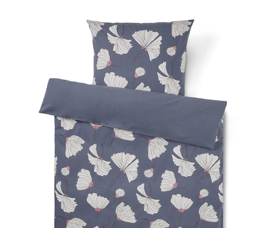 Parure de lit avec un fond bleu foncé et un motif de fleurs blanches aux accents roses. La taie d'oreiller est au-dessus de la housse de couette, dont le bord supérieur est replié pour révéler un revers uni bleu foncé.