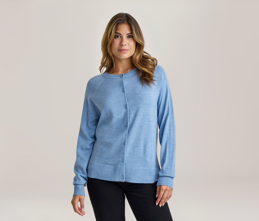 Femme aux cheveux bruns portant un cardigan bleu clair boutonné et un pantalon noir, regardant devant elle.