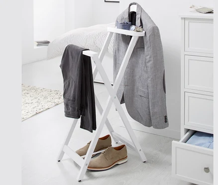 Sur un fond blanc, un valet de nuit sur lequel sont suspendus un blazer gris et un pantalon, et des chaussures marron sont placées en dessous.