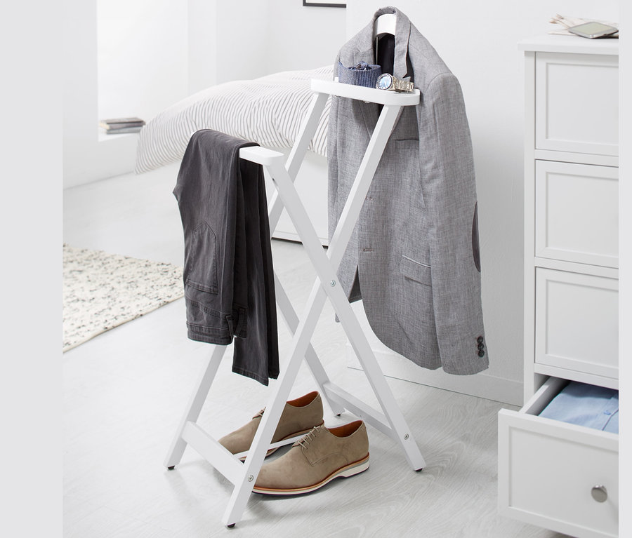 Sur un fond blanc, un valet de nuit sur lequel sont suspendus un blazer gris et un pantalon, et des chaussures marron sont placées en dessous.