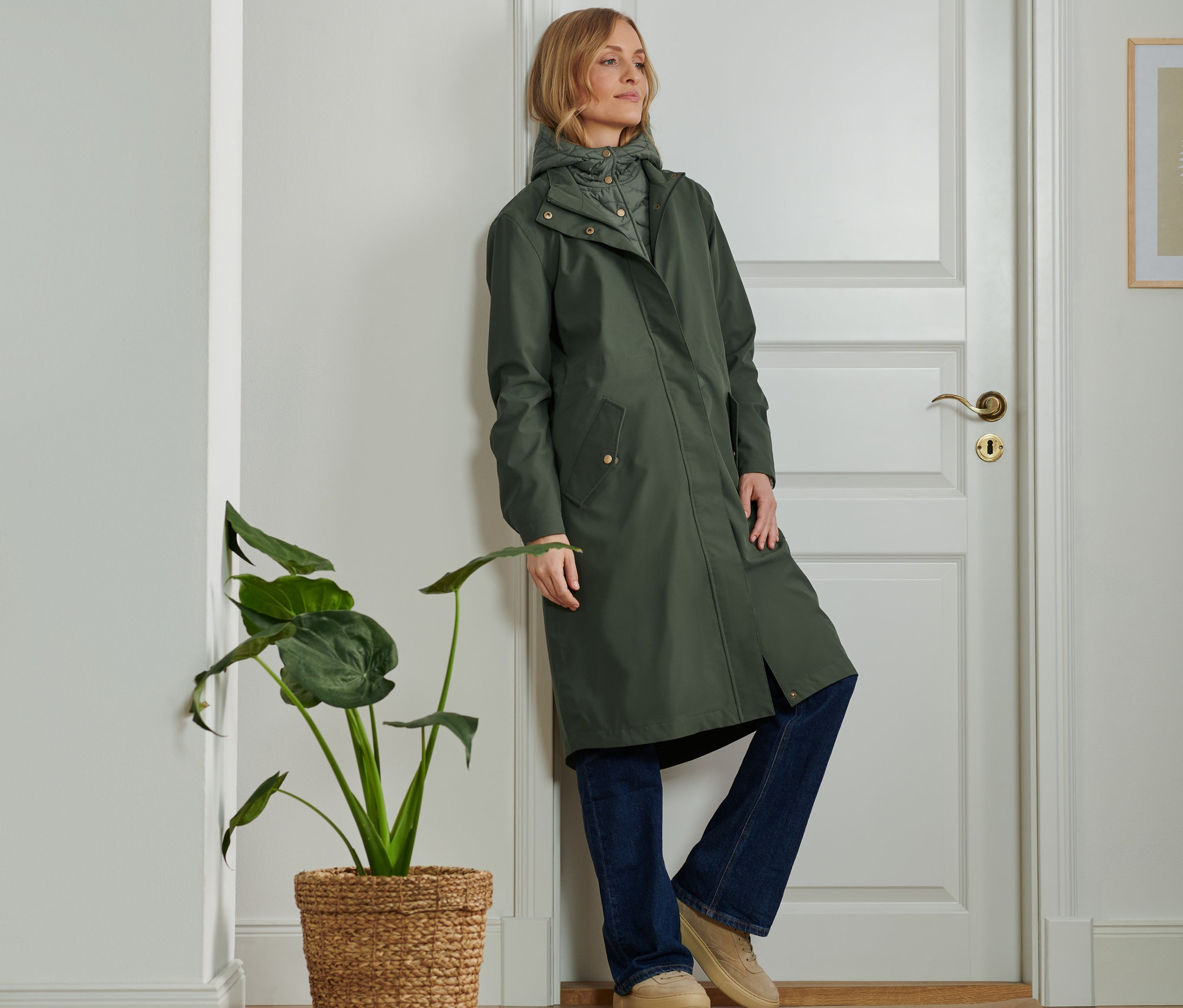 Une femme adossée à une porte porte une Parka d'extérieur 2 en 1.