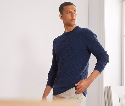 Un homme pose avec un pull en maille bleu chiné.