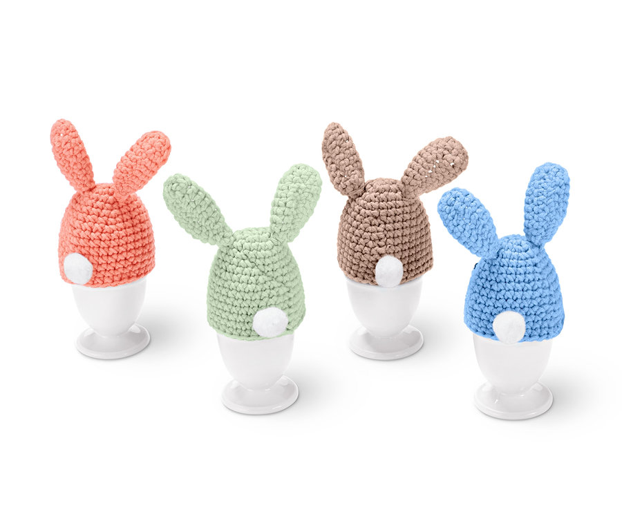 Kit DIY pour couvre-œufs en crochet en forme de lapins de couleurs abricot, vert, beige et bleu sur des coquetiers blancs.