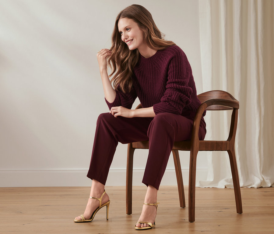 Une femme assise sur une chaise, portant un pantalon en tissu et un pull.