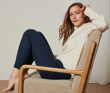 Femme assise dans un fauteuil portant un bas en tricot à motif torsadé.
