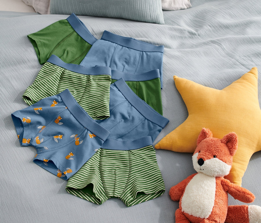 Sur un lit, sept boxers pour enfant de différentes couleurs et motifs sont posés à côté d'une peluche renard et d'une étoile jaune.