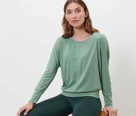Femme assise sur des blocs de bois portant un t-shirt de sport et de yoga vert sauge.