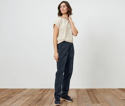 Femme posant en t-shirt beige et pantalon de randonnée fonctionnel bleu marine.
