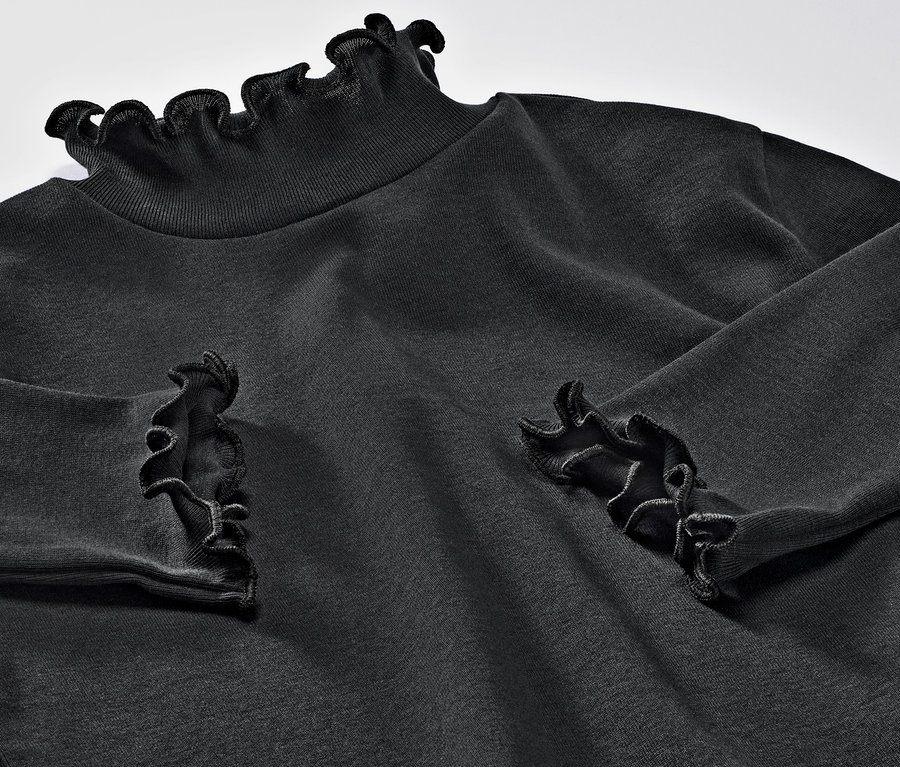 Gros plan sur un t-shirt à manches longues pour enfant avec des volants au col et aux poignets.