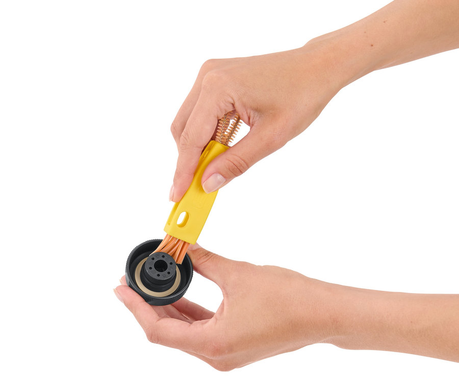 Des mains utilisent une brosse de nettoyage 3 en 1 sur un bouchon noir.