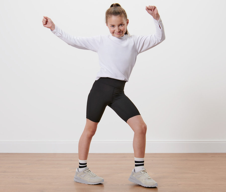 Une fille en chemise blanche et 2 cyclistes de sport pour enfant se tient les bras levés.
