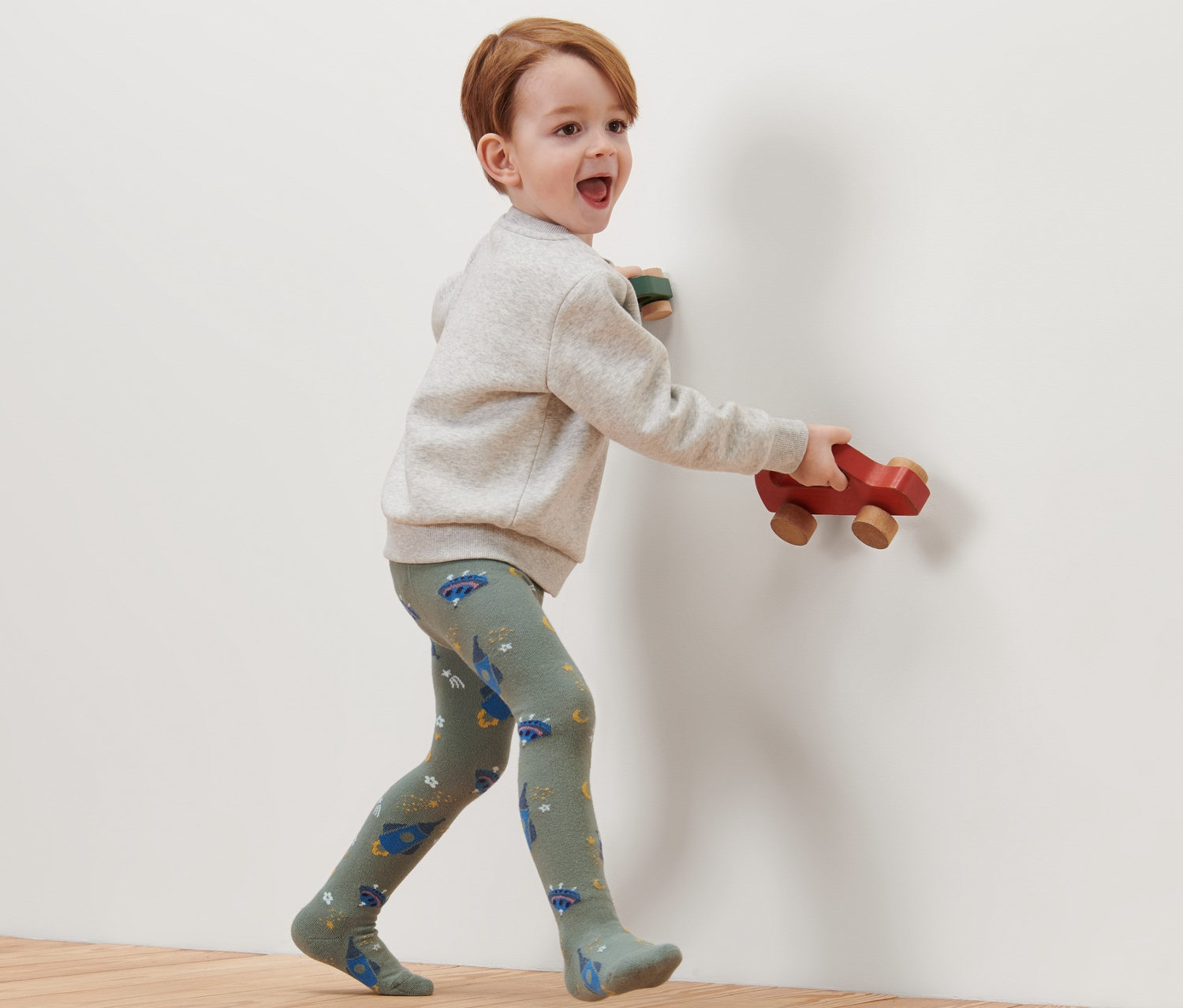 Un garçon marche sur un plancher en bois et porte des collants en coton sur le thème de l'espace.