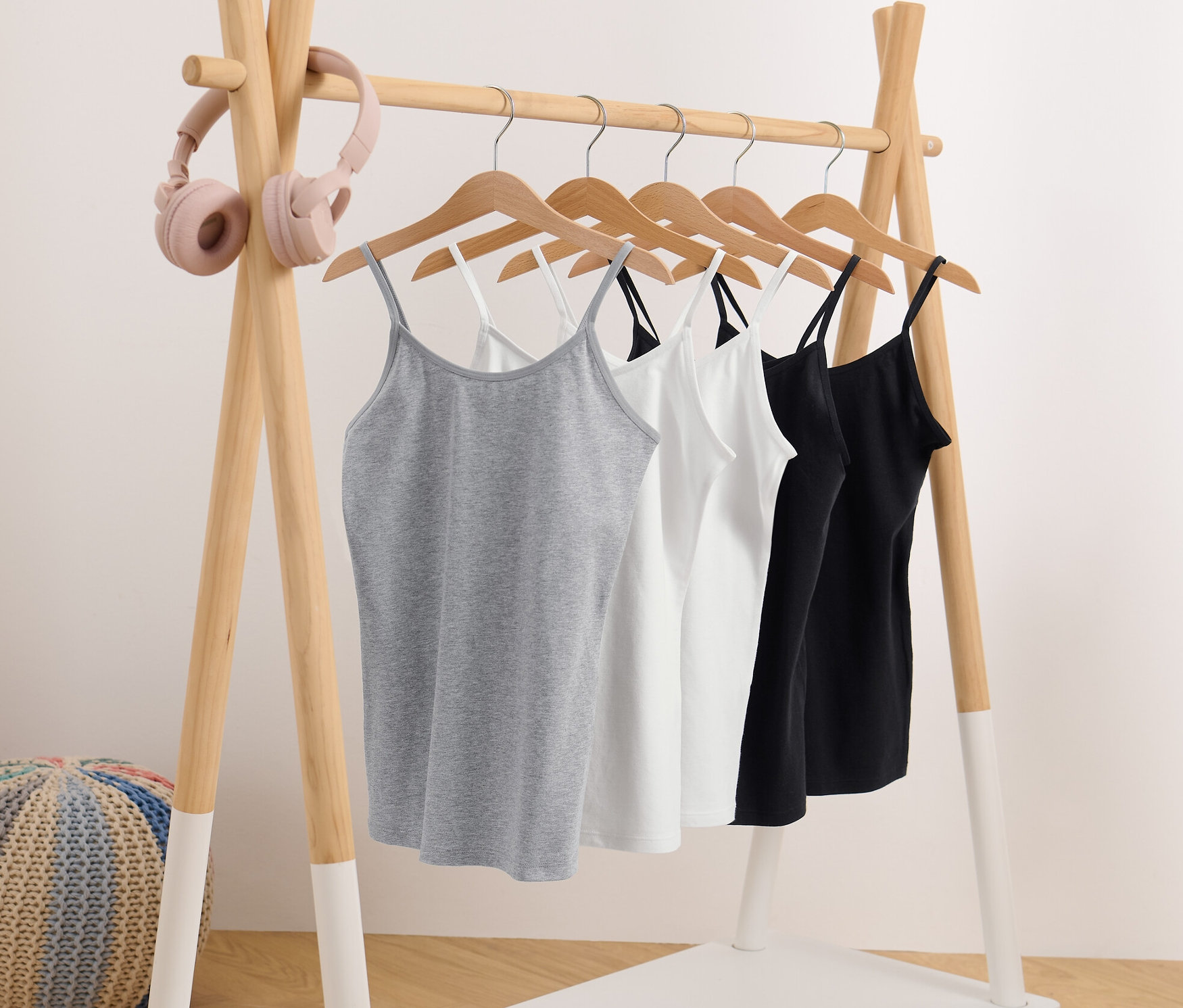 Cinq maillots de corps pour fille gris, blancs et noirs suspendus à une tringle.