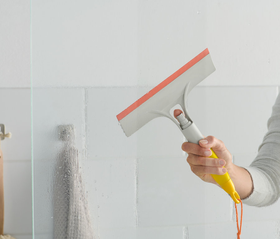 Une femme utilise une raclette 3 en 1 sur une paroi de douche en verre.