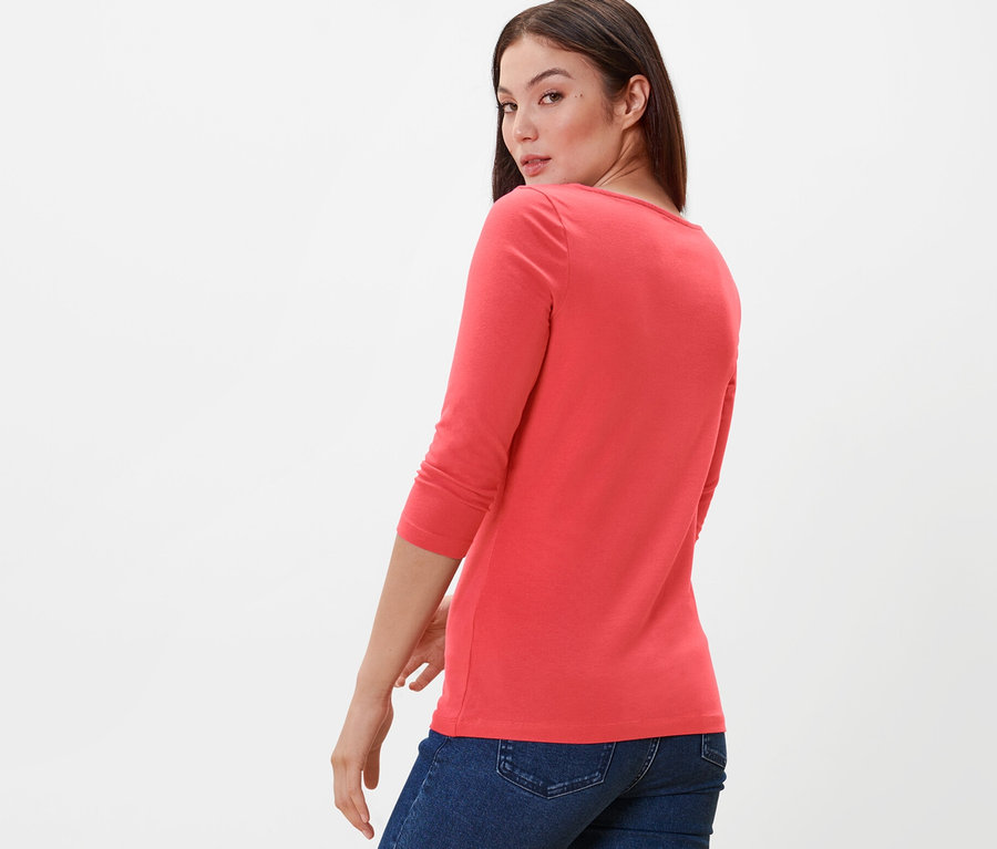 Femme regardant par-dessus son épaule portant un t-shirt corail manches 3/4 et un jean.