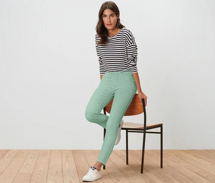 Une femme assise sur une chaise porte un jean coloré coupe « Emma » vert clair.
